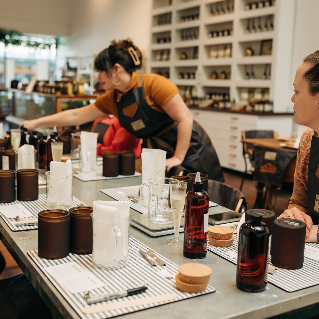 Person working behind a counter with various bottles and glasses in a store setting.