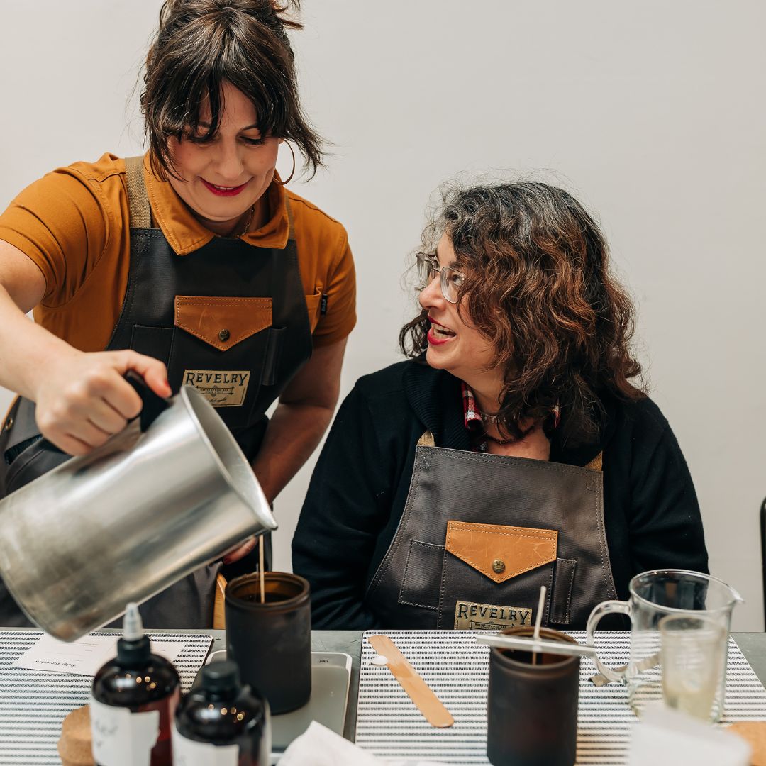 Two women in aprons preparing a drink at a counter.